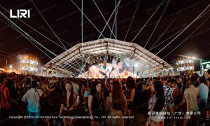 Full-span night view of a 50x30m outdoor festival tent with truss lighting, packed concert crowd, curved white PVC roof