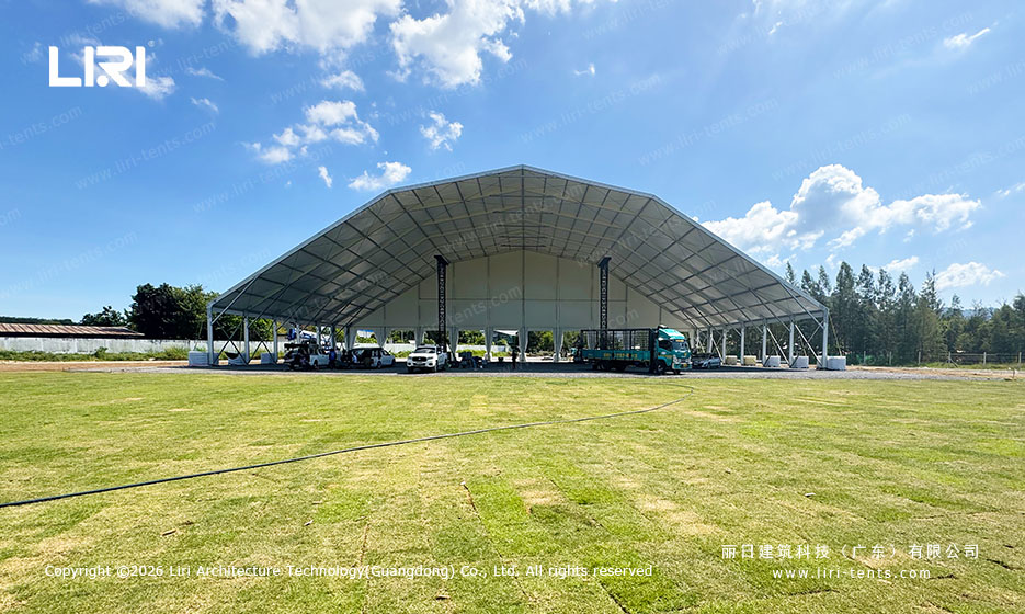Frontal view of a 50x30m arched outdoor festival tent, suspended ceiling visible, vehicles for scale