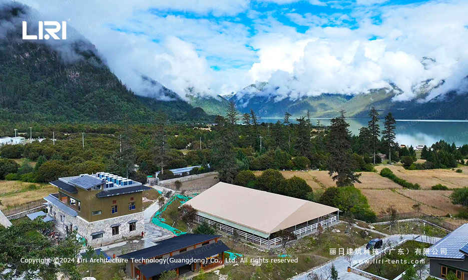 Aerial view of horse arena tent next to alpine lake and stone residence