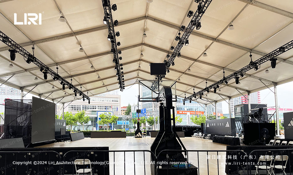 Indoor event tent interior with overhead lighting truss grid and stage equipment