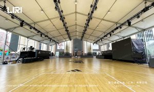 Interior view of a large event tent showing a full basketball court with hardwood flooring and lighting trusses