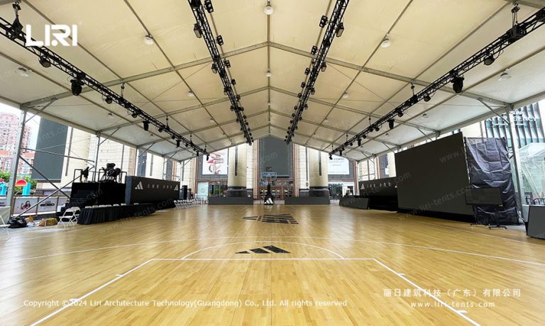 Interior view of a large event tent showing a full basketball court with hardwood flooring and lighting trusses