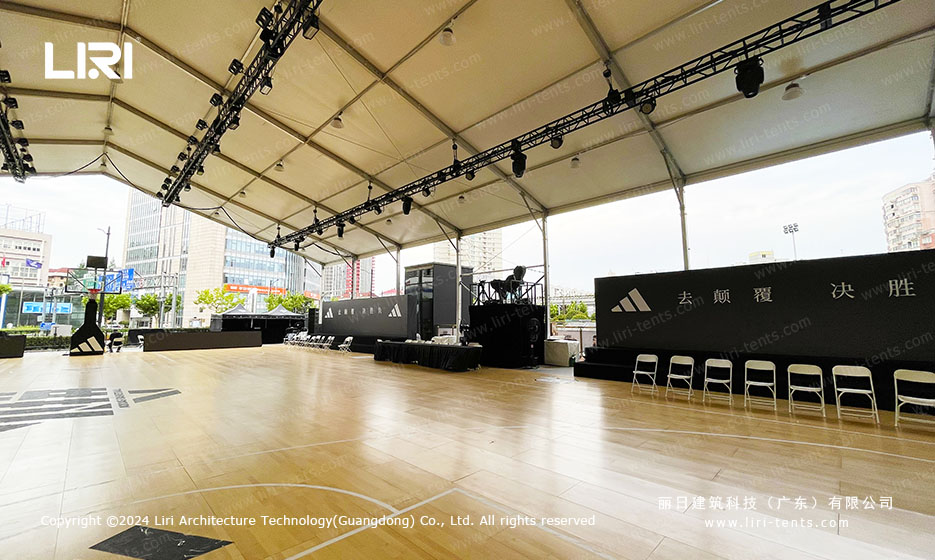 Outdoor party tent interior showing overhead lighting trusses and a fully installed basketball court