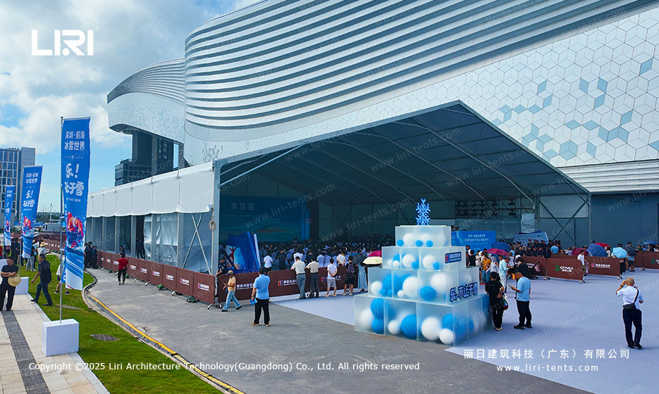 Wide plaza view of an opening ceremony party tent with white A-frame roof and branded banner flags at the entry