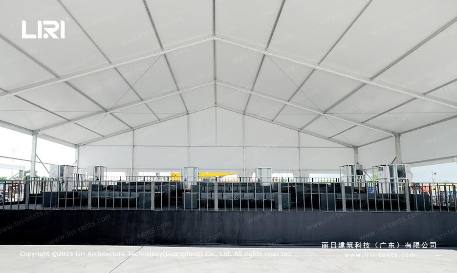 Stage and AV setup at the end of an award ceremony party tent with A-frame rafters and rows of guest chairs