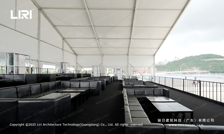 Coastal VIP lounge inside an award ceremony party tent with black sofas and a view of the harbour through the side railings