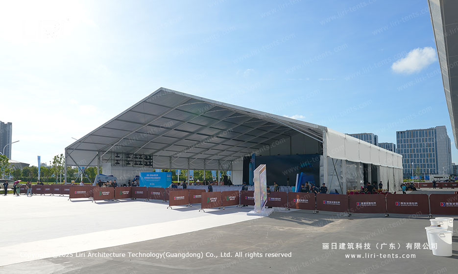 Full long-side exterior of a white A-frame opening ceremony party tent installed on a Shenzhen urban plaza with crowd-control barriers along the perimeter