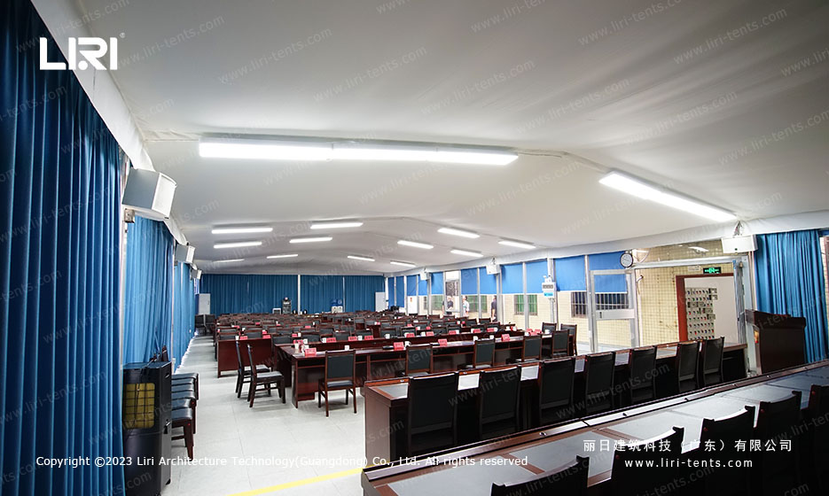 Interior of flat-roof meeting room tent set up with conference seating and blue curtains