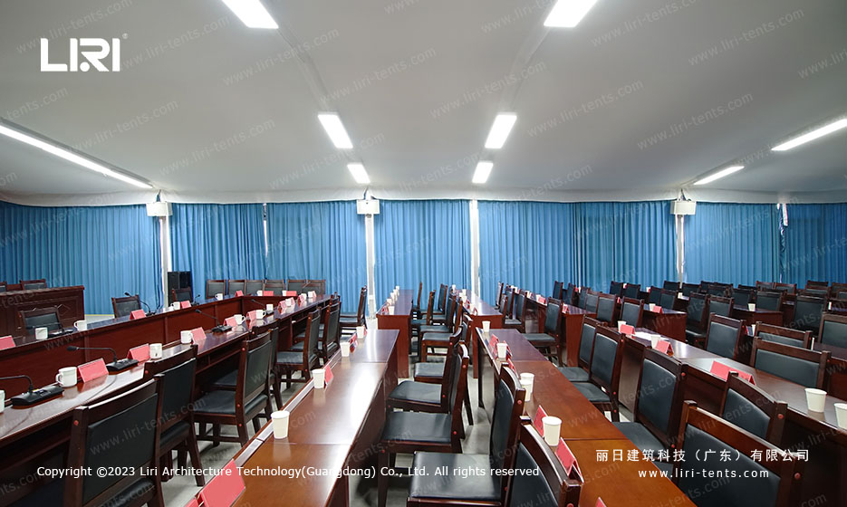 Flat-roof tent dining hall configured for a conference with stage curtain at the front